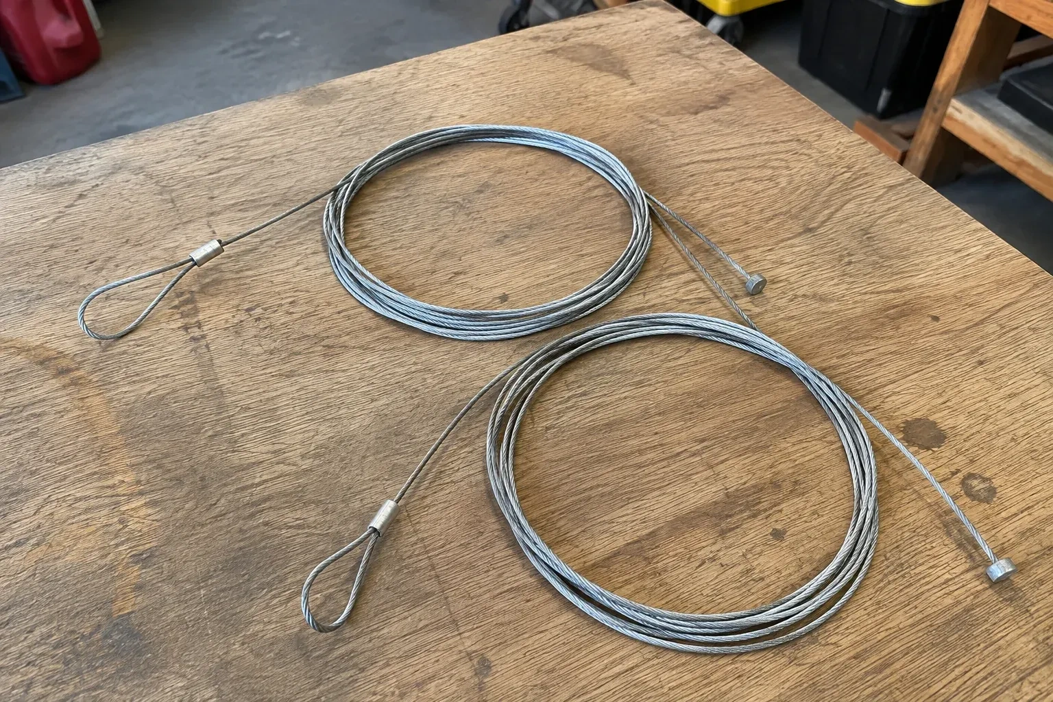 Two coiled steel cables with loop and stop ends on a workbench. — Garage Door Cable Replacement, Toronto
